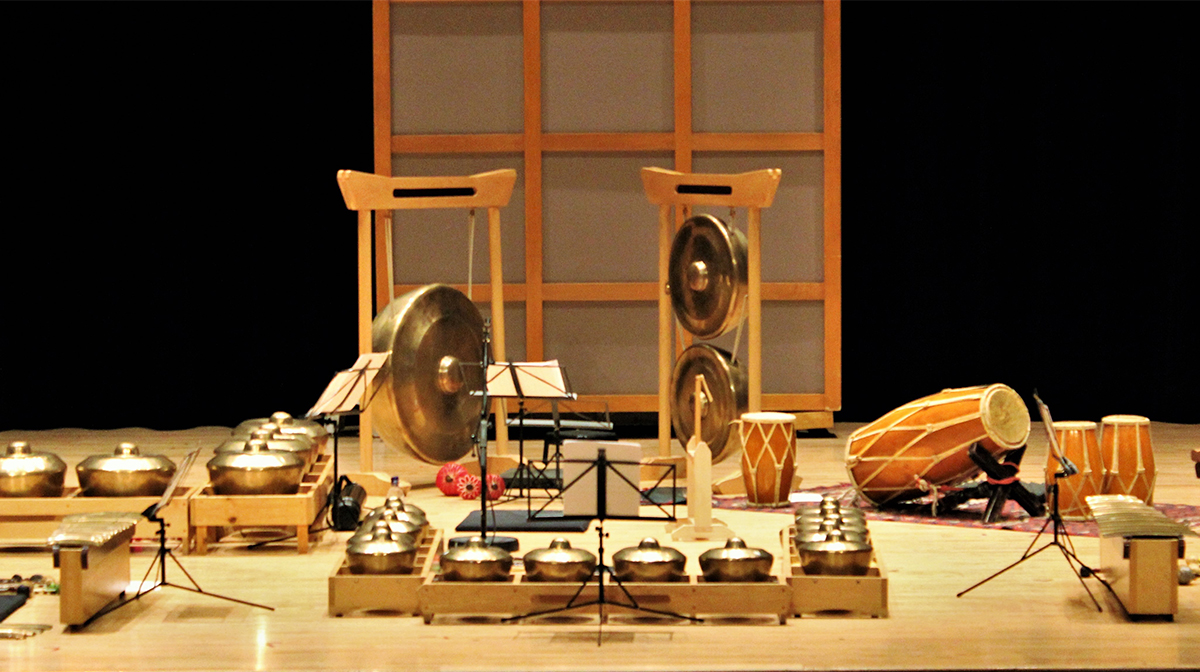 A collection of bronze instruments are displayed on a stage including flutes, gongs, and drums